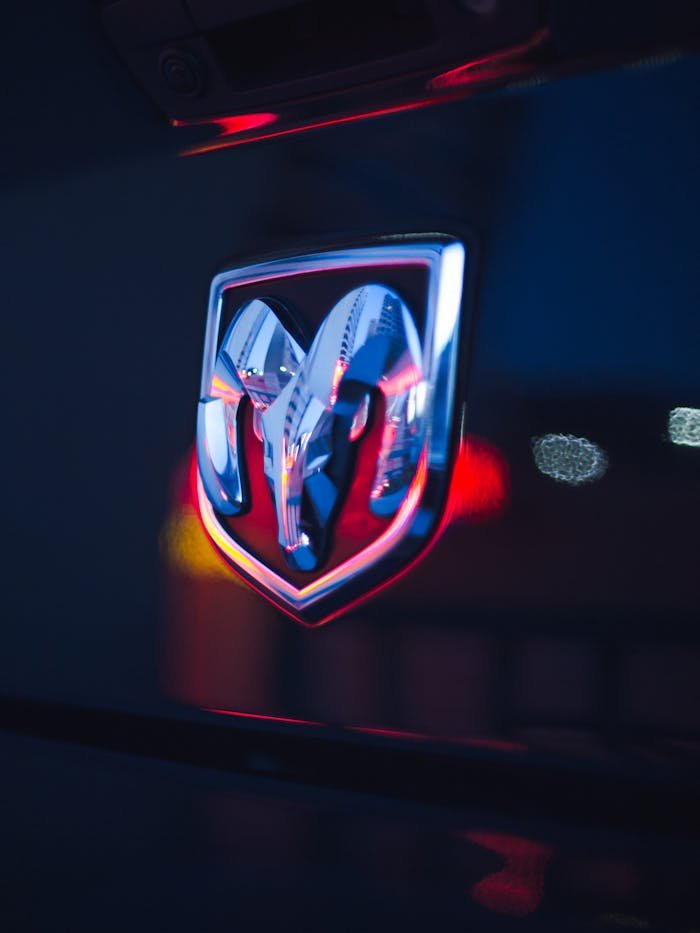Close-up of a chrome Dodge Ram emblem with neon bokeh lighting in the background at night.